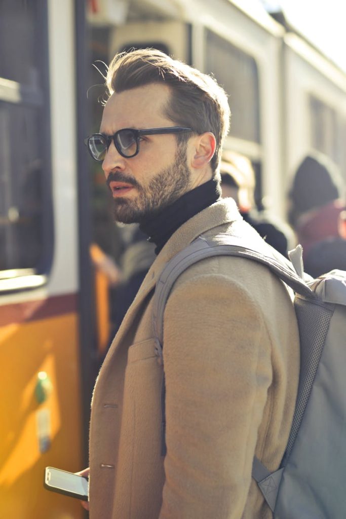 A stylish man with a backpack boards a tram in bustling Budapest, Hungary, during the day.